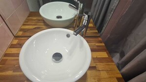 A bathroom with two white ceramic sinks, wooden flooring, and a tiled wall.