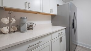 Une cuisine moderne avec des meubles blancs, un réfrigérateur en acier inoxydable, une machine à café et un porte-tasses.
