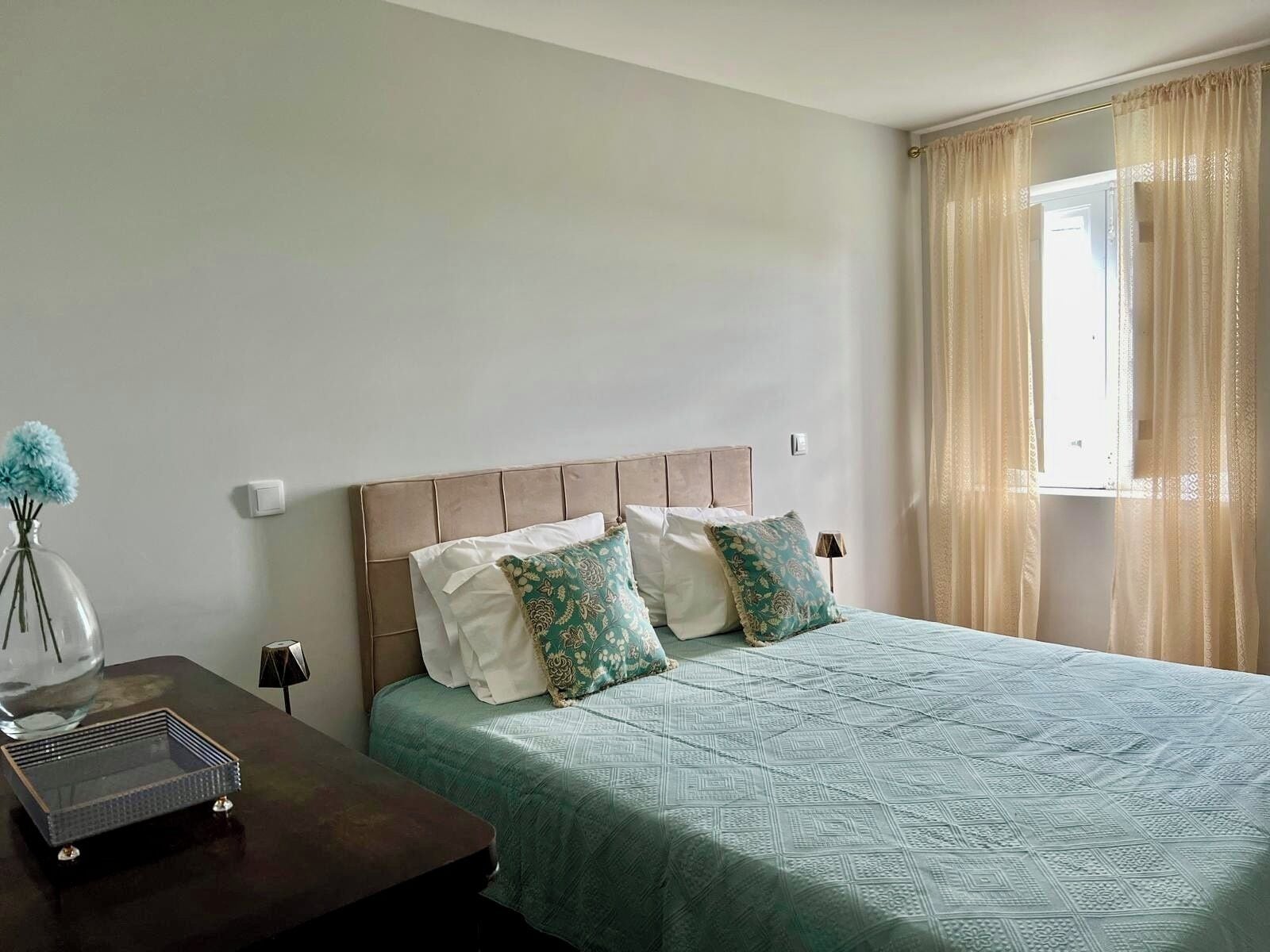 A neatly arranged bedroom with a bed, a bedside table, and a vase with flowers.