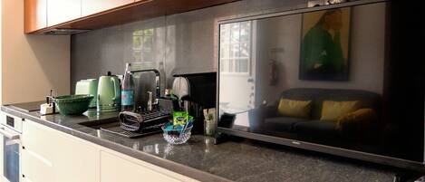 A kitchen with a large flat-screen TV, a coffee maker, a kettle, and a toaster.