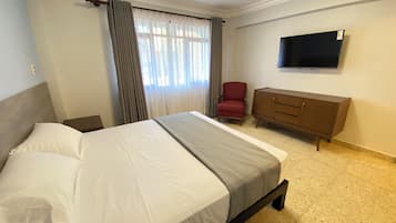 A hotel room with a bed, a red chair, a wooden dresser, and a flat-screen TV on the wall.