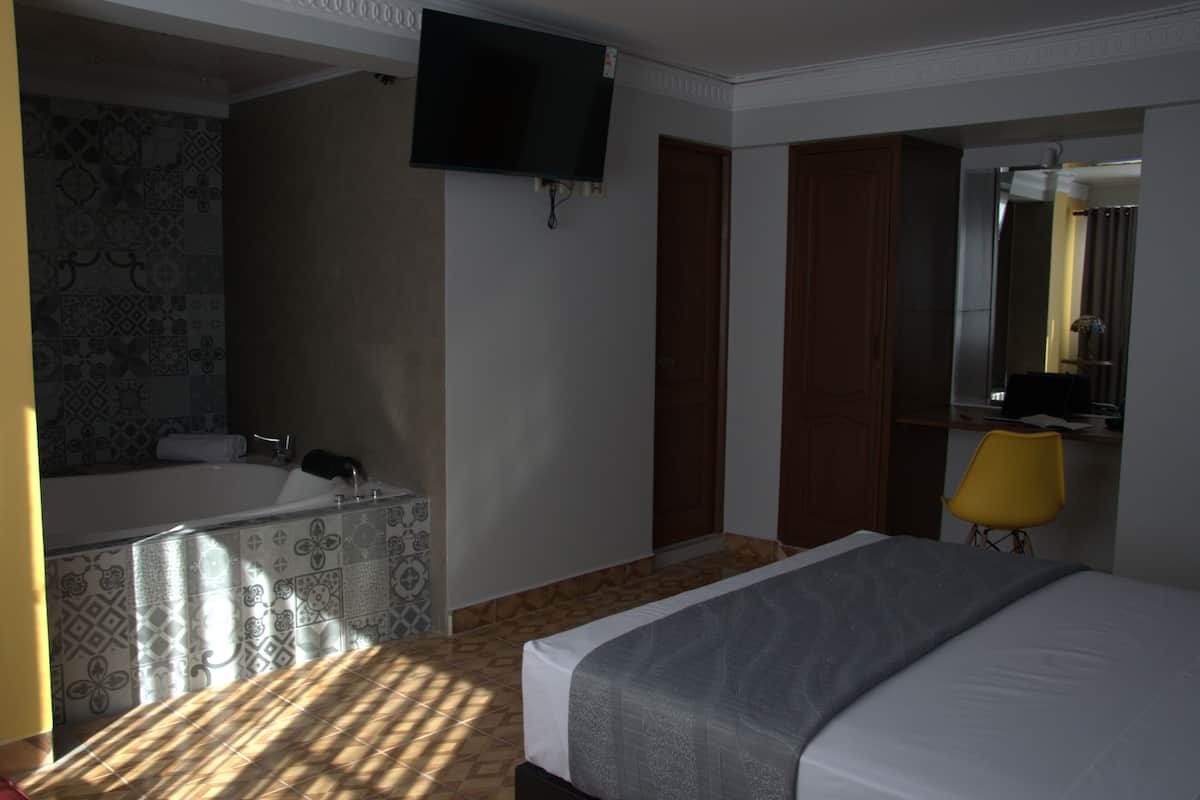 Habitación de hotel con cama, televisión montada en la pared, baño con bañera y una silla amarilla.