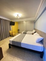 Una habitación de hotel con una cama grande, un televisor montado en la pared y una silla.