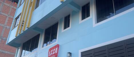 Un edificio de varios pisos con fachada azul claro, un letrero rojo que indica 'IZZA HOTEL' y un amplio portón de garaje.