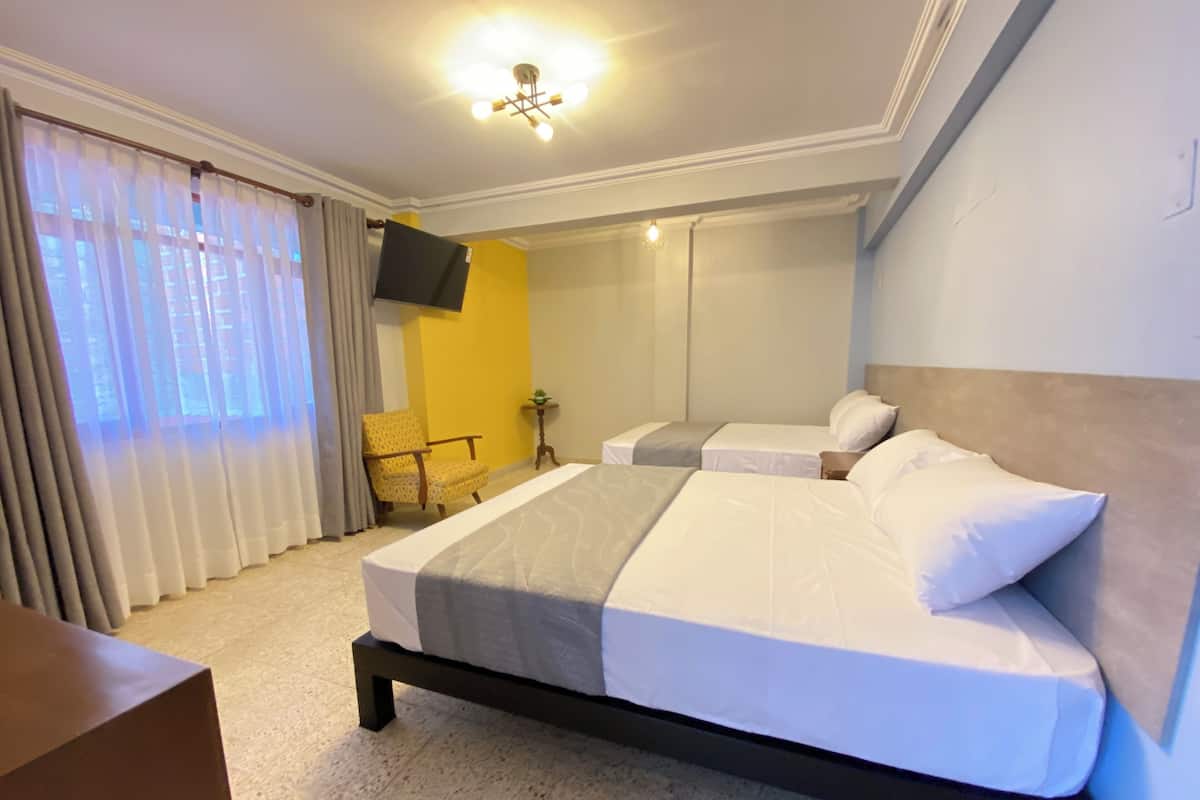 Habitación de hotel con una cama grande, una silla, una mesita y un televisor fijado a la pared.