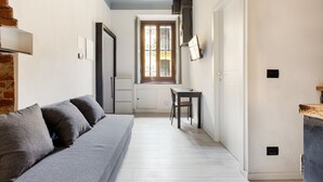 A narrow hallway with a sofa, a small table, and a window with decorative ironwork.