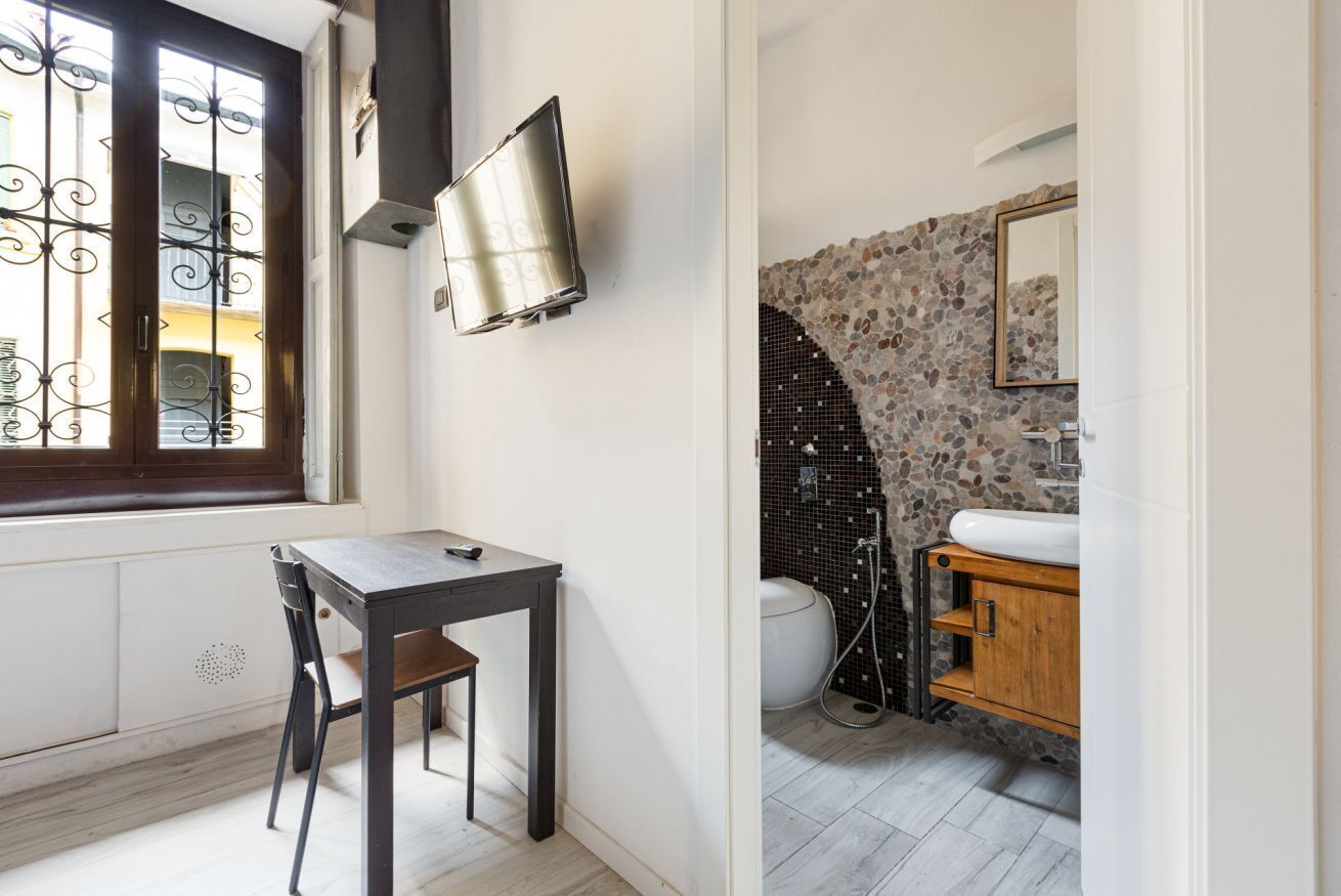 Een kleine kamer met raam, een tafel, een stoel, een wastafel en een douche.