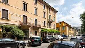 A street view with parked cars, a yellow building with balconies, and a clear sky.