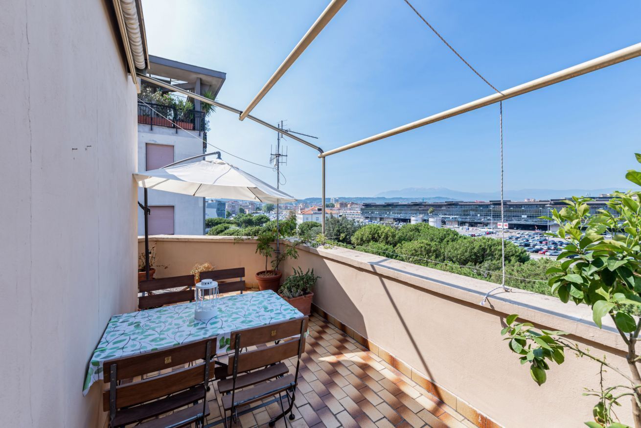 Ein Balkon mit Tisch und Stühlen, Blumentöpfen und Blick auf die Stadt.
