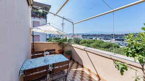 A balcony with a table and chairs, potted plants, and a view of a cityscape. - GuestHost - Bright apartment that accommodates up to 4 people, equipped with all the comforts for a pleasant stay, with two bedrooms and a panoramic terrace that offers a beautiful view of the Maiella and Gran Sasso mountains. The accommodation is locate (Pescara)
