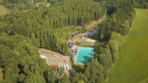 Vista aerea di un resort con piscina, parcheggio per camper e cabine circondate da dolci colline boscose.