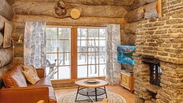 A log cabin interior with a stone fireplace, a leather sofa, a round table, and a television.