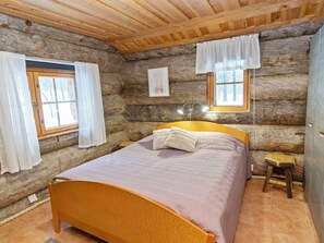 Une chambre dans une cabane en rondins, avec un lit, des rideaux, un petit tabouret et une fenêtre.