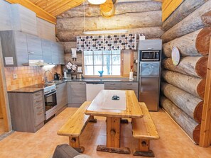 Une cuisine rustique aménagée dans une cabane en rondins, avec une table en bois, un four encastré, un réfrigérateur et une fenêtre offrant une vue agréable.