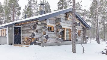 A log cabin with a snow-covered roof, wooden windows, and a door.