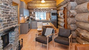Interior acolhedor de uma cabana de madeira, com lareira de pedra, mesa de jantar de madeira e área de estar.