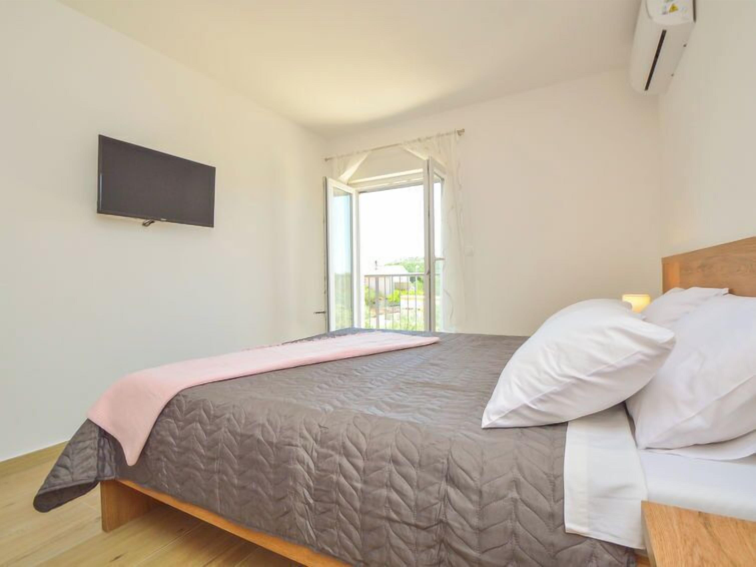 A bedroom with a bed, a TV mounted on the wall, and a balcony with a view.