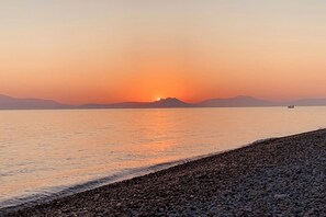A sunset over a calm sea with a pebbled shore and distant mountains. - Stunning Greek Villa-private pool-beach-sleeps 8 (Sykia)