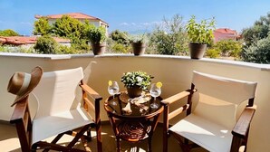 A balcony with two wooden chairs, a table with a potted plant, and two glasses of water.