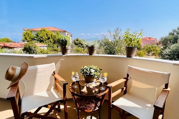 Ein Balkon mit zwei Holzstühlen, einem Tisch mit einem Blumentopf und zwei Gläsern Wasser.