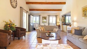 A spacious living room with a sofa, armchairs, a coffee table, and a clock on the wall.