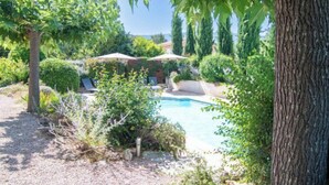 A pool area with lounge chairs and umbrellas, surrounded by greenery and trees.