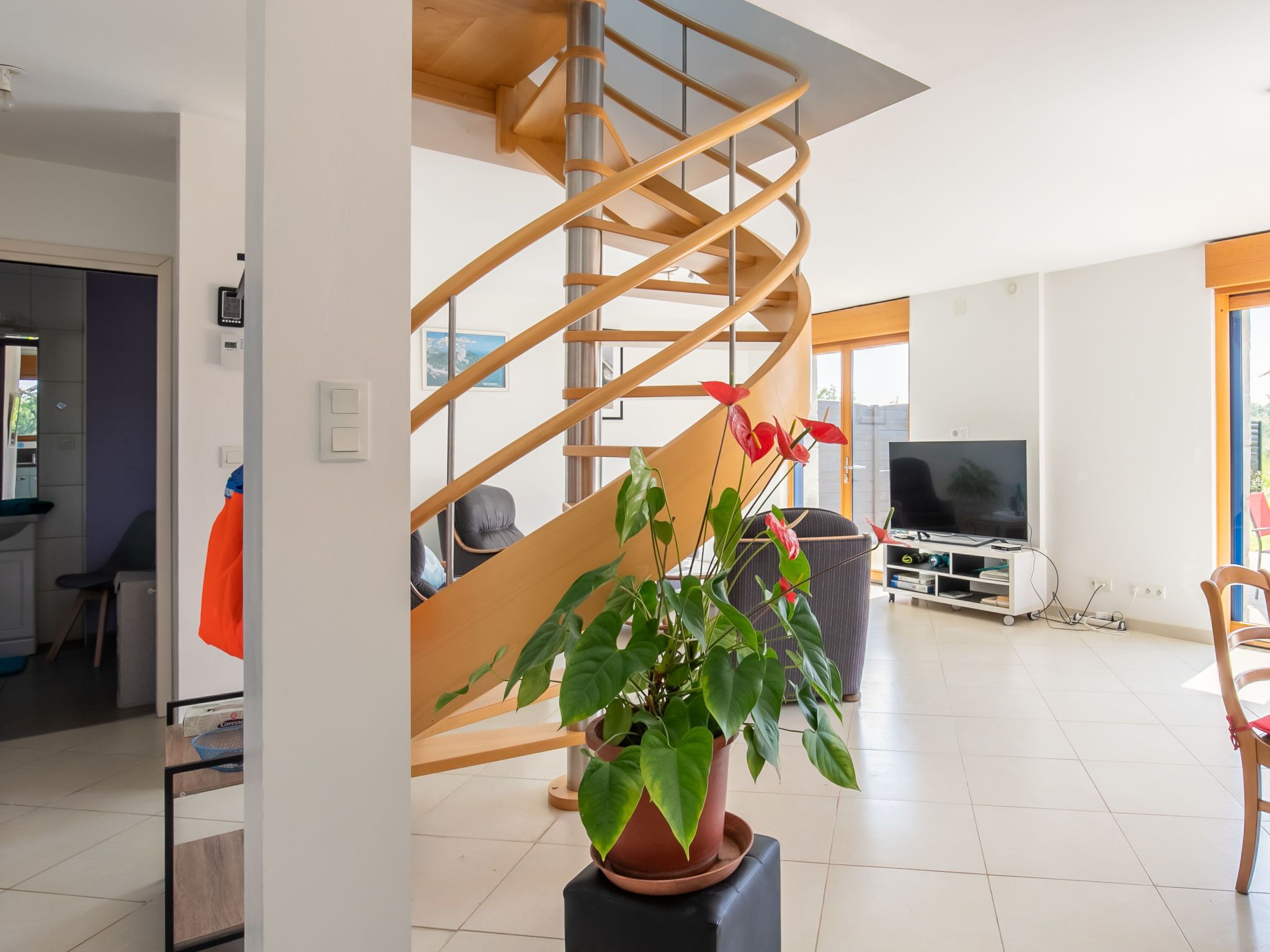 A modern living room with a spiral staircase, a potted plant, a television, and a seating area.