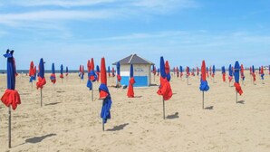 Una playa con hileras de sombrillas rojas y azules, un puesto de socorristas y una playa de arena.