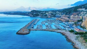 A marina with boats docked, a rocky breakwater, and buildings along the coastline. - Panorama by Interhome (Altea)