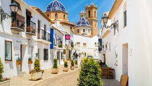A narrow street with white buildings, a blue-domed church, and a bell tower. - Panorama by Interhome (Altea)