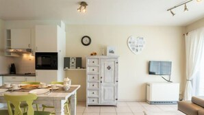 A modern kitchen with white cabinets, a microwave, and a dining area with a table and chairs. - Green Garden VX 105 with pool view by Interhome (De Haan)