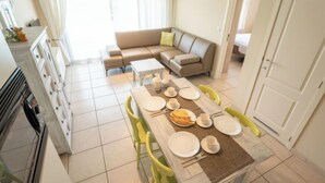 A modern kitchen with a dining area, a sofa, and a view of the outdoors. - Green Garden VX 105 with pool view by Interhome (De Haan)