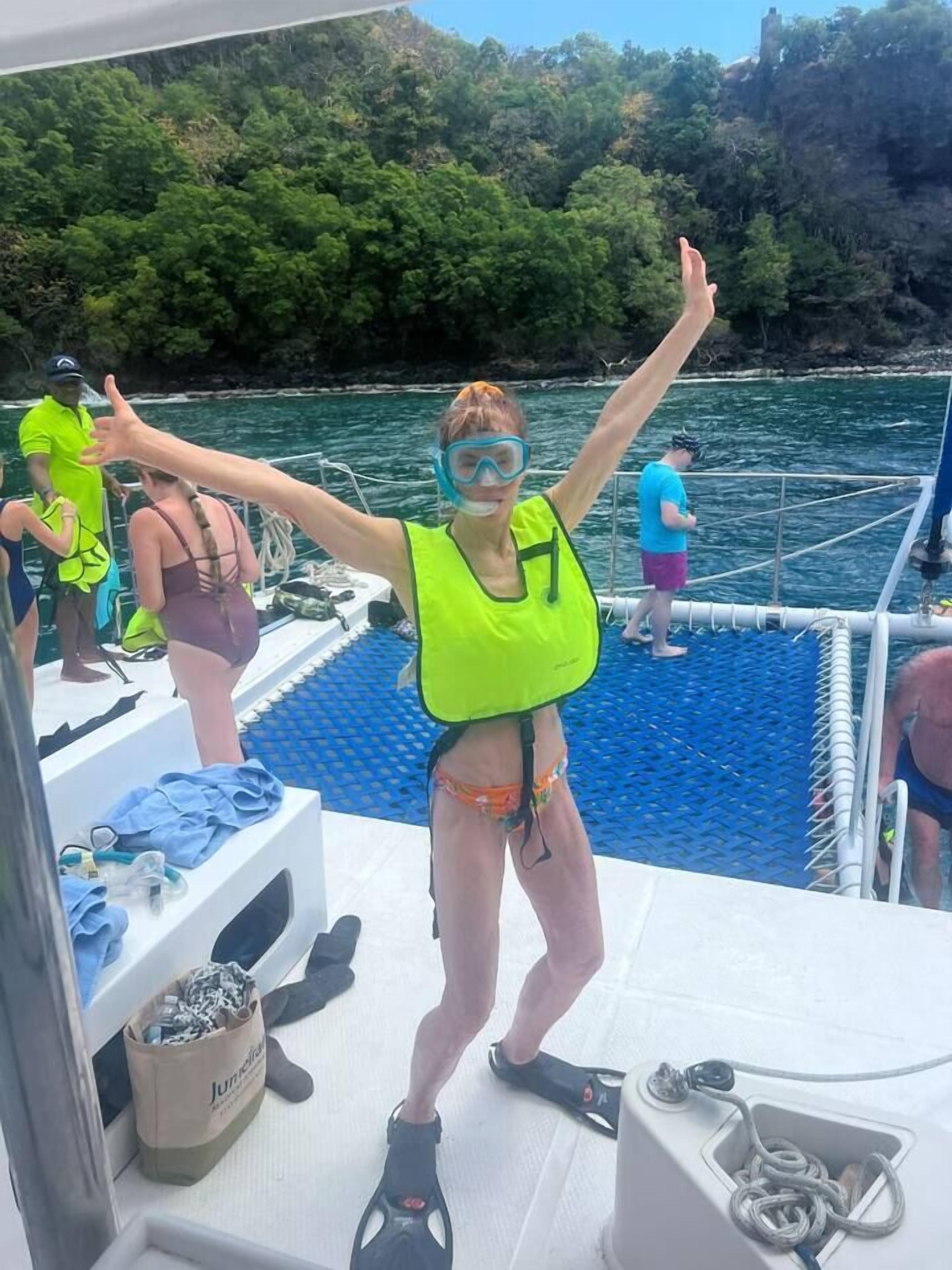 A person on a boat wearing a life jacket and a harness, with a bag labeled "Jungle" and a rope coiled on the deck.