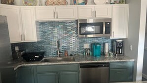A kitchen with white cabinets, a stainless steel microwave, and a blue tiled backsplash. - Beach House Kids & Pets OK Oct, Nov, Dec DISCOUNTED! AMIsland White Sand Beaches (Bradenton)