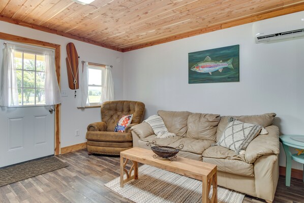 A cozy living room with a wooden ceiling, a brown leather armchair, a beige sofa, a wooden coffee table, and a fish painting on the wall. - Norfork Studio by White River: Ideal for Fishing! (Norfork)