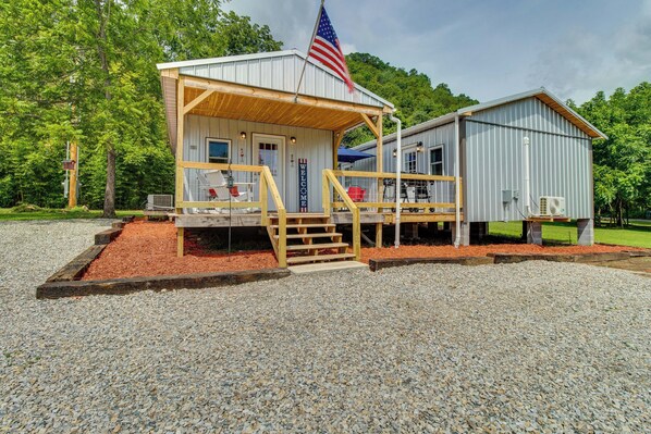 A rustic cabin with a wooden porch, a flagpole with an American flag, and a 'Welcome' sign.