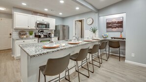 A modern kitchen with white cabinets, stainless steel appliances, and a granite island with bar stools. - Atlanta Getaway w/ Private Yard: Near Airport (Atlanta)
