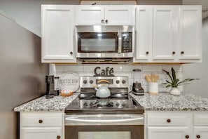 A kitchen with white cabinets, a stainless steel microwave, a coffee maker, and a kettle.