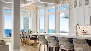 A modern kitchen with white cabinetry, a large island with bar seating, and a view of the ocean.