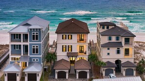 A coastal residential area with three houses, each featuring a garage and a balcony. The houses are built on a sloped terrain with a view of the ocean.