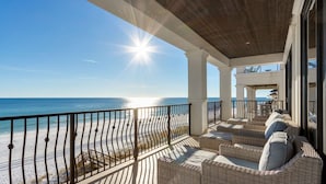 A balcony with wicker furniture overlooking a beach and ocean.