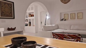 Un soggiorno moderno con un divano bianco, un tavolino in legno con due ciotole, una sedia colorata in vimini e un mobile contenitore bianco con diversi oggetti.