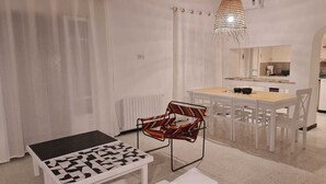 Un soggiorno moderno con zona pranzo, caratterizzato da un tavolino da caffè decorato, una sedia particolare e una lampada a sospensione.