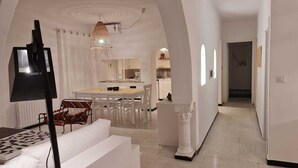 Un interno moderno con zona pranzo, divano, lampada e cucina sullo sfondo.