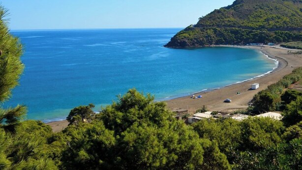 Paesaggio costiero con spiaggia, mare cristallino e una montagna sullo sfondo.