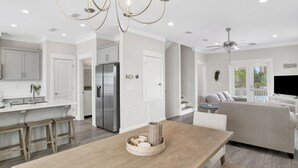 Une cuisine moderne avec des meubles blancs, un réfrigérateur en acier inoxydable et un coin repas comprenant une table en bois et des tabourets.