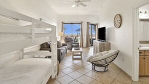 Una habitación con literas, un sofá, una silla, un televisor y una zona de cocina.