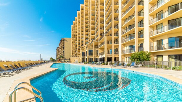 Un hotel con una piscina grande, varios balcones y tumbonas.