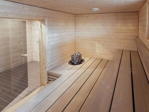 Un sauna en bois doté d’une zone de douche carrelée et d’un foyer central.