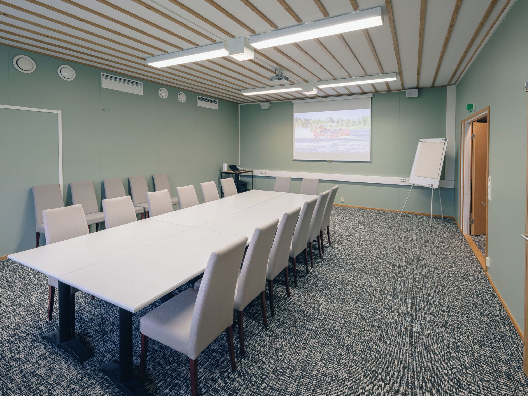 Een vergaderruimte met een lange tafel, stoelen, een scherm voor een beamer en een whiteboard.